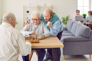 Group of happy men senior people playing chess in nursing home sitting at the table. Pensioners...