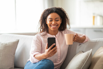 Woman with coffee cup using smartphone at home