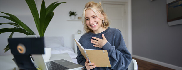 Portrait of young smiling blond woman, working from home, online chatting, using digital video...