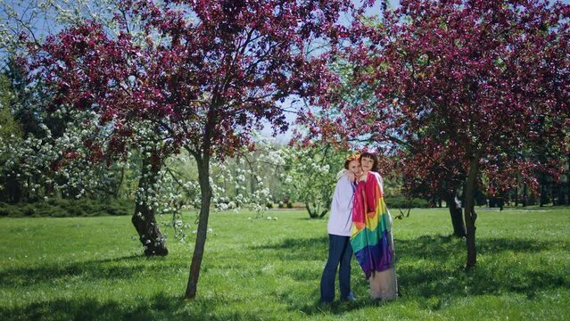Very lovely lgbt couple hugging each other in the park in front of the camera they holding the lgbt rainbow flag in hands