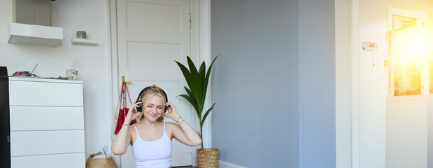 Portrait of young woman at home, connects to online gym training session, following fitness...