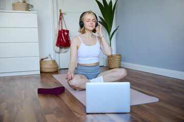 Portrait of fit and healthy woman at home, practice yoga, sitting on rubber mat, listening to instructions online, using meditation music to relax, following guidance on laptop