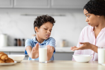 Boy rejecting glass of milk in kitchen scene