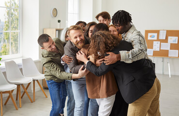 Diverse group of people in an office comes together in a embrace, symbolizing support, unity, and a...