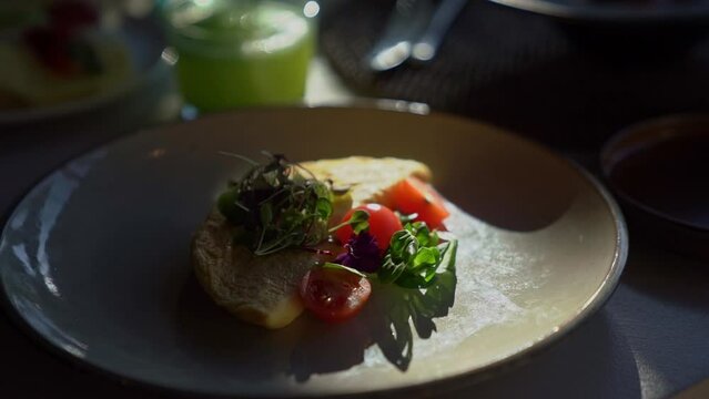 Breakfast omelet with vegetables stands on the table in the rays of the sun