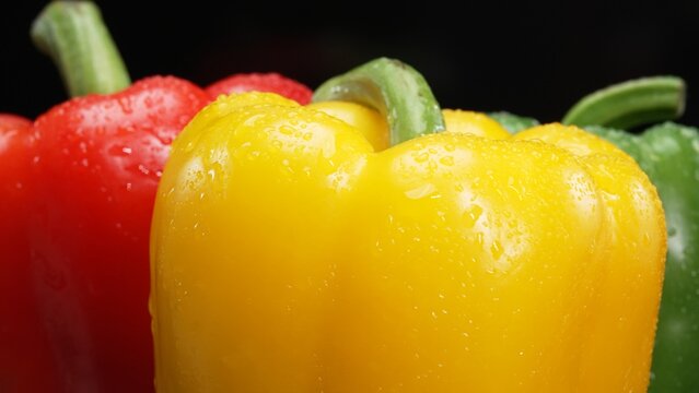 Macro of fresh bell peppers in this stunning macrography against a black background. Each close-up shot captures the rich hues, intricate textures, and captivating details of bell peppers. Comestible.