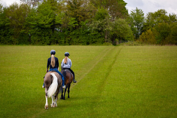 Two young girls horse riding across a field, Image shows the rear view of 2 girls in their 20's hacking out their horses one being a section D palomino Welsh cob stallion and the other a bay Connemara