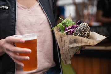 Close up of woman hands holding delicious organic salmon vegetarian burger and homebrewed IPA beer on open air beer an burger urban street food festival in Ljubljana, Slovenia