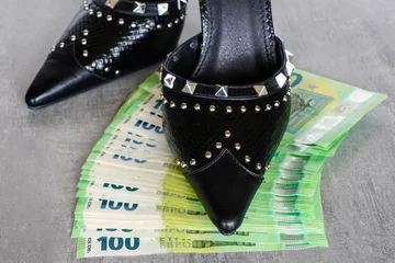 Foto op Plexiglas Black women's shoe with metal spikes on money bills, symbol of greed, leadership and dominance © Zigmunds