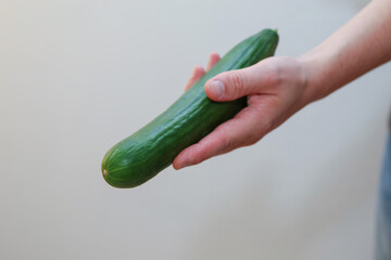 A Caucasian man holds a green long cucumber in a hand - white background