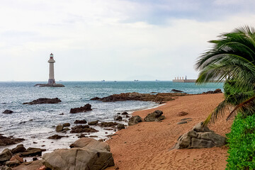View of a lighthouse in the sea near a rocky shore with palm trees. Heavenly Grottoes Park, Sanya.