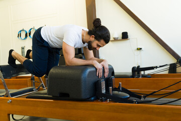 Hispanic man working out on a pilates reformer machine - 792034066