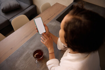Rear top view of young adult woman holding a smartphone with blank white mockup touch screen,...