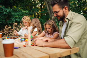 Young happy fun family playing board game in nature at picnic table.