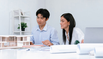 Professional male asian architect using ruler to measure house model length while young beautiful...