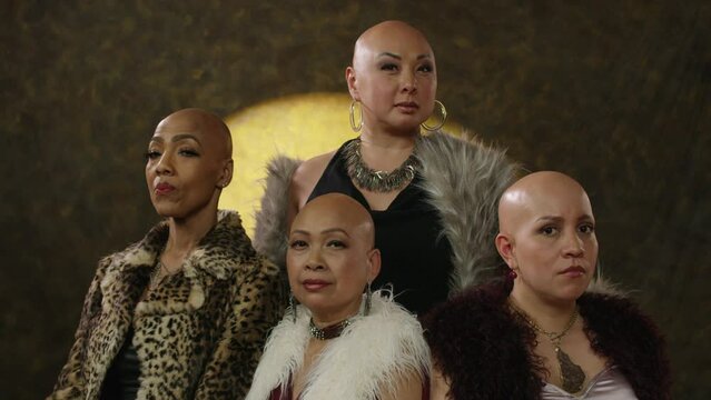 Four bald women look at the camera in sync on a gray background