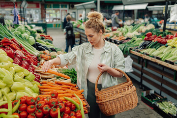 Obraz premium Shopper with wicker basket selecting organic carrots at green market.