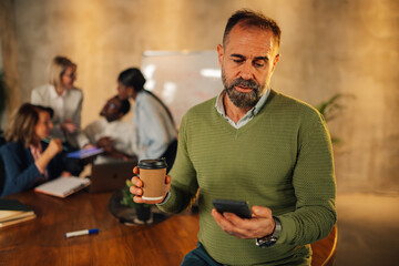 Manager with coffee cup typing on phone on meeting of interracial staff