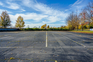 A parking lot with no cars parked in it. The sky is blue and there are trees in the background