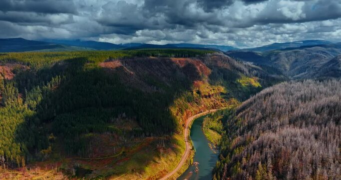 Huge grey dramatic clouds throwing shadows on the bare mountains in Oregon State, the USA. Narrow blue river flows between the rocks. Top view.