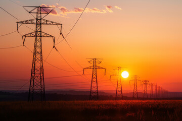 A sunset over a field with a line of power lines. The sky is orange and the sun is setting