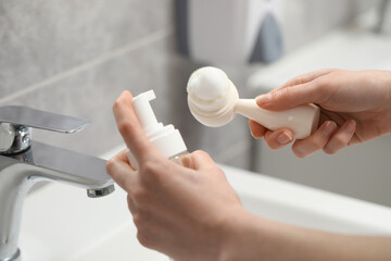 Washing face. Woman applying cleansing foam onto brush above sink in bathroom, closeup