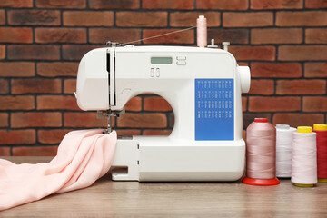 Sewing machine with fabric and spools of threads on wooden table against brick wall
