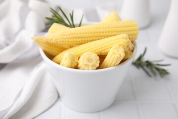 Tasty fresh yellow baby corns in bowl on white tiled table