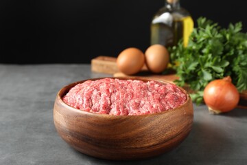 Raw ground meat in bowl and different products on grey table