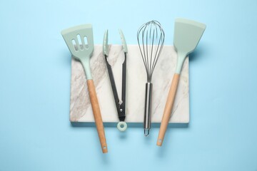 Different spatulas, whisk and tongs on light blue background, flat lay