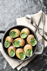Delicious cooked snails in baking dish served on grey textured table, flat lay