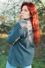 Beautiful red-haired woman enjoying smell in a flowering blooming spring garden. Spring blossom