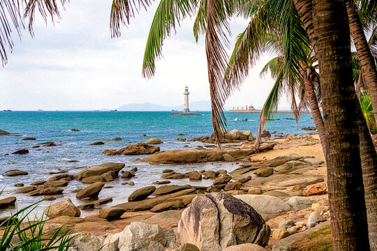 View of a lighthouse in the sea near a rocky shore with palm trees. Heavenly Grottoes Park, Sanya.