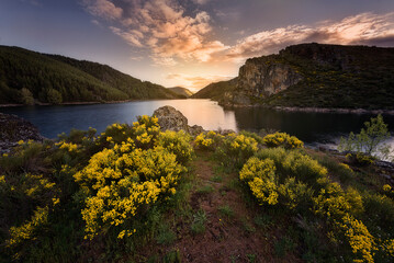 Sunset at the Camporredondo reservoir with warm colored clouds in the sky in Alba de los Cardaños,...