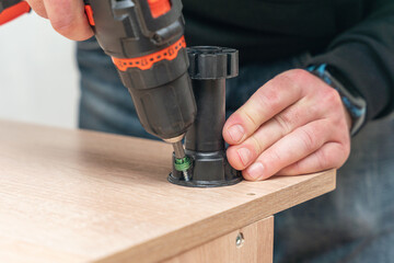 Assembling furniture, a man screws a plastic leg with a screwdriver
