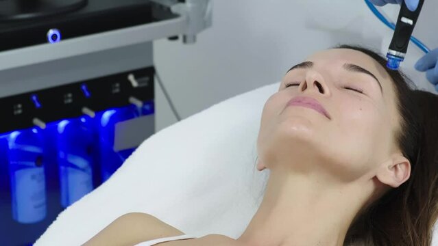 Beautician in gloves conducts vacuum cleaning and polishing face skin of young woman in cosmetology clinic. Professional moisturizing and rejuvenating hardware procedures for modern people.