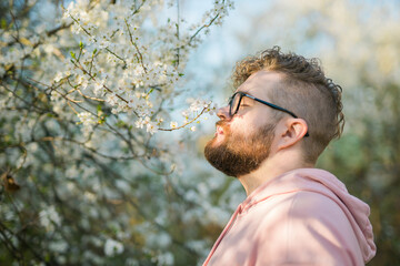 Portrait of curly millennial man inhales the fragrance of spring flowers of blooming jasmine or...