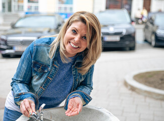 Joyful Woman Leaning Over Outdoor Fountain in Denim Jacket