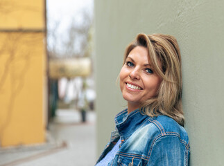 Confident Woman Leaning on Wall in Denim Jacket Outdoors