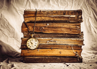 Pile of old dusty books with broken pocket watch on dirty white cloth.