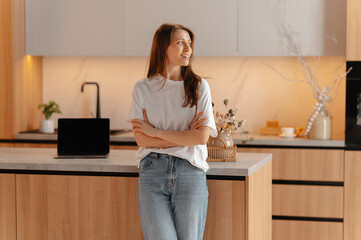 Wide smiling young woman is standing with arms folded in her brand new kitchen.