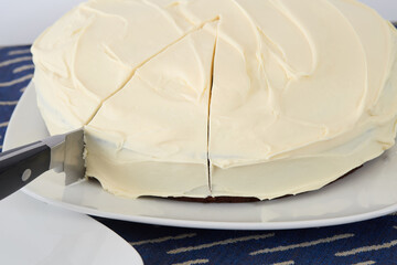 Round dark chocolate cake with delicate white frosting, with a slice cut into it.