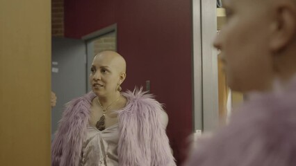 Woman with alopecia looks in the mirror at herself while wearing a furry coat