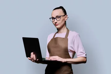 Foto op Plexiglas Portrait of 30s woman in apron holding laptop on grey background © Valerii Honcharuk