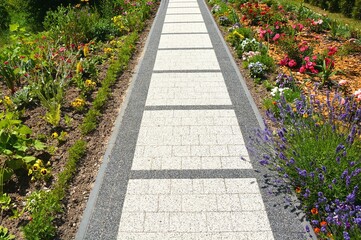 Stoneware walkway in between garden of flowers and plants lined with decorative bark on the ground