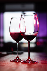 Silhouette of two glass glasses with red wine inside on a wooden table, indoors.
