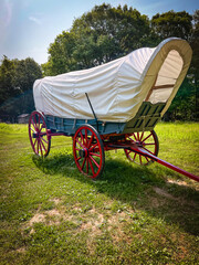 Side view of a 19th century style horse-drawn carriage or covered wagon set against a green rural...