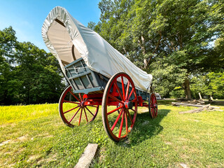 Rear view of a 19th century style horse-drawn carriage or covered wagon set against a green rural...