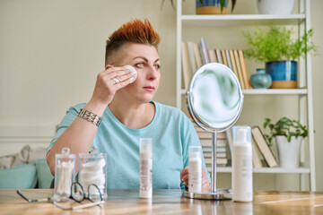 Middle-aged woman with a mirror taking care of her facial skin