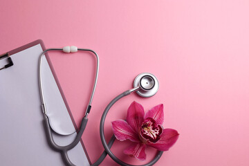 Orchid and stethoscope on a colored background, top view. Symbol of women's health and gynecology.